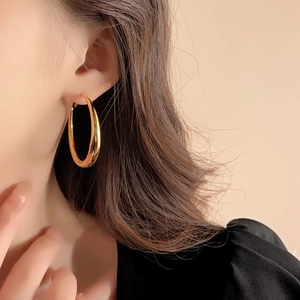 Close-up of a model wearing large golden geometric hoop earrings with polished metal finish