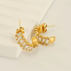 Close-up of gold C-shaped earrings with rectangular zircons in a claw setting