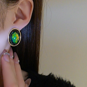 Gros plan d'une boucle d'oreille géométrique en opale verte avec cadre doré sur un modèle