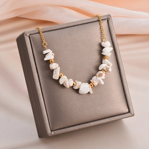 Detail of bohemian necklace with irregular white stones and gold beads on silk fabric