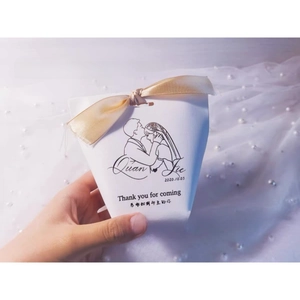 Detail of white wedding favor box with gold ribbon bow and custom couple illustration