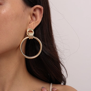 Close-up of a large gold geometric hoop earring with a knotted top detail on a model