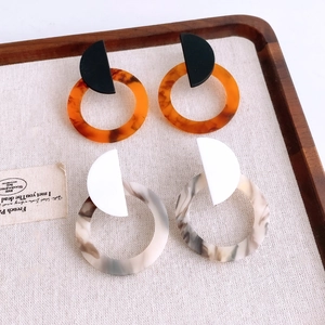 Flat lay of retro geometric acrylic earrings with amber and marble patterns on wooden tray