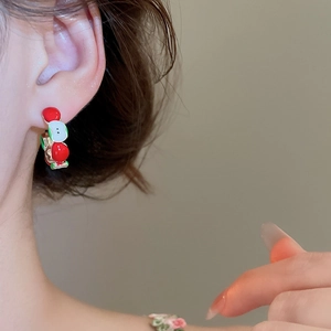 Close-up of a model wearing C-shaped apple earrings with red and white enamel finish