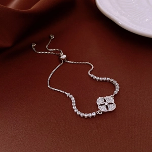 Macro shot of silver clover bracelet with zircon inlay on brown satin backdrop