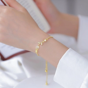 Detail view of gold tulip bracelet with opal petals on a woman's wrist with book