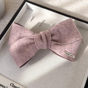 Detailed macro view of a handmade Morandi pink wool felt bow hair clip with gold logo tag