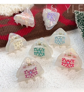 Close-up of snowflake hair claws in pearlized candy colors on a cozy winter backdrop