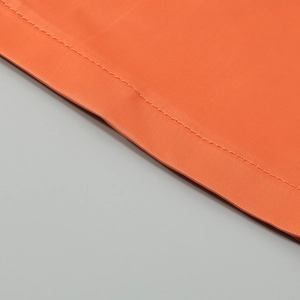 Close-up of orange fabric stitching and smooth textile texture on a jumpsuit