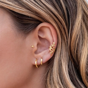 Close-up of gold ear cuff set featuring leaf clip, hoops and studs on model ear
