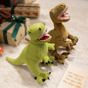 Cute green and brown Tyrannosaurus Rex plush toys in a warm festive gift setting