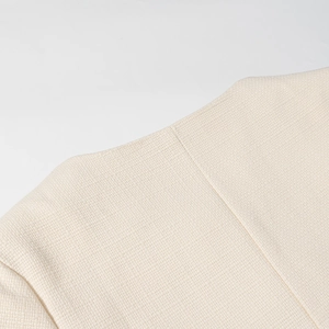 Dettaglio ravvicinato della trama in tweed beige e cuciture su giacca corta