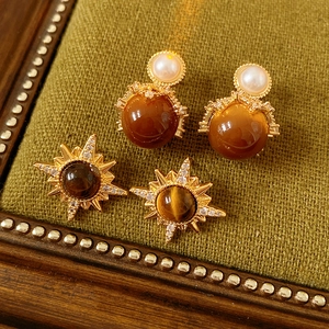 Detail view of gold starburst and round tiger eye stud earrings on green velvet pad