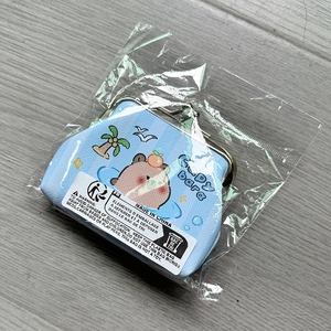 Close-up of a blue Capybara coin purse in clear plastic packaging on a grey wooden floor