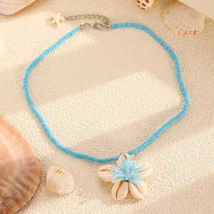 Detailed view of ocean style beaded necklace with shell pendant on a sandy beach