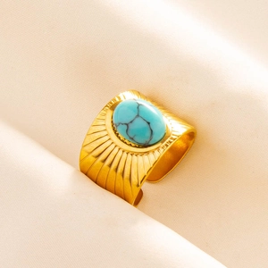 Macro detail of 18K gold stainless steel ring with turquoise stone on beige fabric