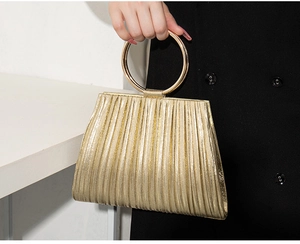 Detail of golden pleated evening clutch bag with round metal wrist handle for women