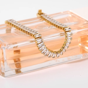 Bracciale tennis dorato con zirconi rettangolari adagiato su una boccetta di profumo