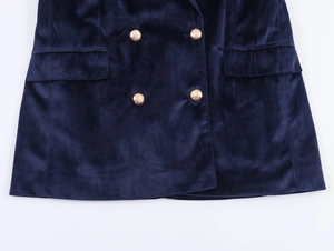 Detailed close-up of dark blue velvet blazer with gold embossed buttons and flap pockets