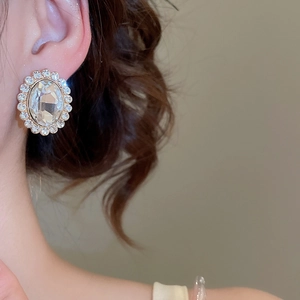 Close-up of vintage oval rhinestone stud earrings with gold finish on a model