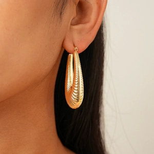Close-up of golden oval hoop earrings with horizontal ribbed texture on female model