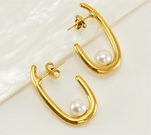 Macro shot of 18K gold U-shaped earrings with inlaid white pearls on a textured background