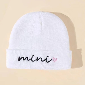 Close-up of white knitted beanie featuring mini text and pink heart embroidery