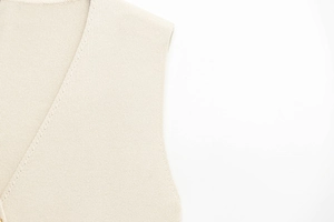 Détail du gilet en tricot beige montrant la texture fine et les coutures de l'encolure