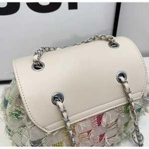 Close-up of woven tweed texture with fringe details and silver chain on a denim style bag