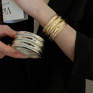 Detail of irregular wave texture on wide metallic bangles in gold and silver finish