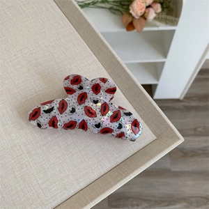 Detail of white acrylic hair claw clip featuring red lip and black bat prints
