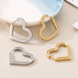 Close-up of gold and silver heart earrings with CNC zircon inlay on a ceramic plate
