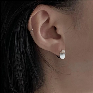 Close-up of minimalist brushed silver oval stud earrings worn on female earlobe