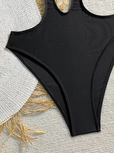 Detail of black cutout swimsuit showing high-cut leg and fine stitching on woven mat