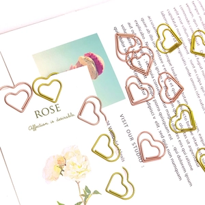 Rose gold and gold heart-shaped paper clips scattered on a book and artistic cards