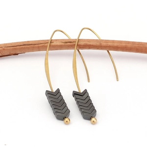Detailed view of vintage hematite arrow earrings with gold hooks on a wooden branch