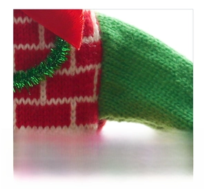 Detail of red and white brick pattern knitted Christmas wine bottle cover with green sleeves