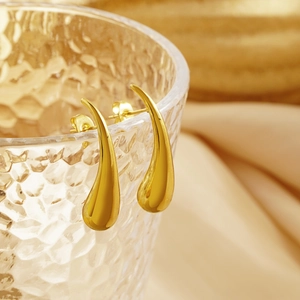 Close-up of golden teardrop earrings with mirror finish hanging on a glass rim