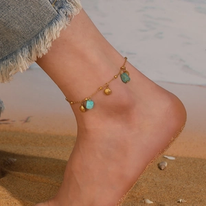 Close-up of a gold seashell and turquoise anklet worn on the ankle at the beach