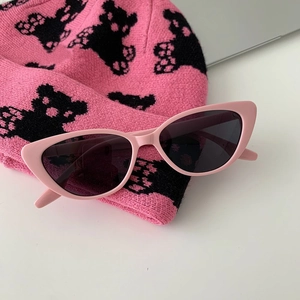 Detailed view of pink cat-eye sunglasses with dark lenses on a pink knit surface