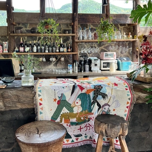 Bohemian woven camping blanket with colorful illustrations and tassels on a wooden table