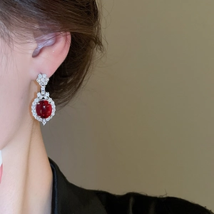 Macro shot of oval ruby red earrings with shimmering diamond-encrusted floral halo