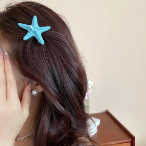 Detail showing a blue starfish hair clip styled on wavy brown hair for a beach look