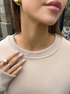 Detail of model wearing chunky golden heart earrings and a textured irregular band ring