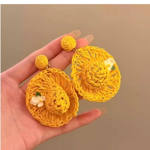 Detailed macro view of yellow raffia woven sun hat earrings with white flower petals