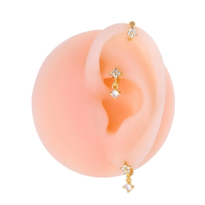 Dettaglio di tre orecchini a cerchio dorati con zirconi su un modello di orecchio in silicone