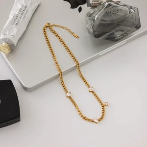 Détail du collier gourmette doré avec trois pierres de zircon cubiques sur un bureau