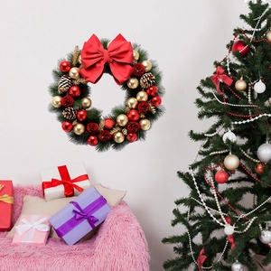 Close-up of Christmas wreath with red bow, pine cones, and gold ornaments on a white wall