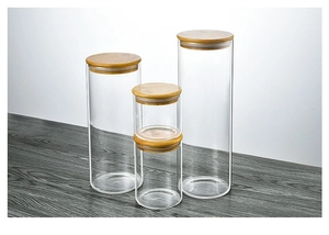Set of 4 glass storage jars with bamboo lids in different sizes on dark wood table
