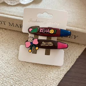 Detailed view of two dark reddish-brown resin hair clips with cartoon motifs on a card